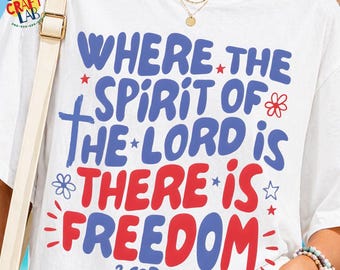 May include: White t-shirt with a patriotic design. The shirt features the text "WHERE THE SPIRIT OF THE LORD IS THERE IS FREEDOM" in blue and red, with decorative stars and flowers. The Bible verse 2 COR. 3:17 is at the bottom.