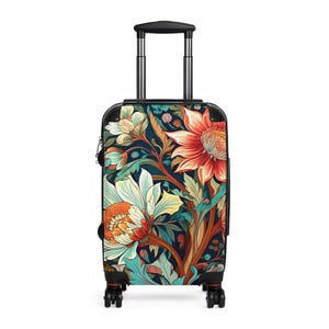 Könnte beinhalten: Ein Rollkoffer mit dunkelblauem Hintergrund und einem lebendigen Blumenmuster aus großen orangefarbenen, roten und weißen Blüten mit grünen Blättern. Das Gepäckstück hat einen schwarzen Rahmen, einen ausziehbaren silbernen Griff und vier Rollen.