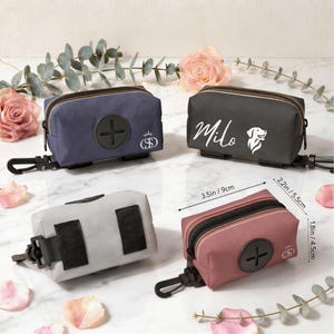 May include: Four rectangular waste bag dispensers in navy, black, light gray, and dusty rose. Each features a black zipper, a black plastic clip, and a circular rubber opening. The black bag displays the name Milo and a dog icon. Dimensions are 3.5in by 2.2in by 1.8in.