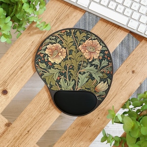 May include: A round mouse pad with a black wrist rest featuring a botanical pattern of light orange flowers and green foliage on a dark background. The mouse pad has a smooth surface and a curved bottom edge designed to support the wrist during use.