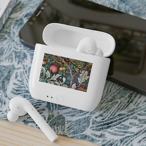 May include: A white wireless earbud charging case with an open lid, featuring a rectangular floral and fruit pattern on the front. One white earbud rests inside the case, and another white earbud lies on the surface next to the charging case.