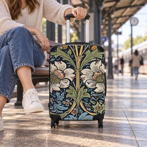 May include: A rectangular rolling suitcase featuring a detailed botanical pattern with large cream-colored flowers, green foliage, and blue accents on a dark background, equipped with a black telescopic handle and four swivel wheels.