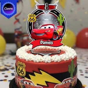 May include: A red cake decorated with a Cars theme. The cake features a red Lightning McQueen topper with the name "Daniels" on a red banner. The cake is decorated with white frosting, Route 66 signs, and a cactus.