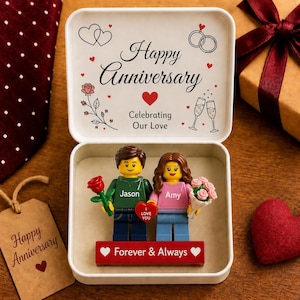 May include: A white box with the words "Happy Anniversary" and "Celebrating Our Love." Inside are Lego figures of a couple, with the names "Jason" and "Amy." A red base reads "Forever & Always."