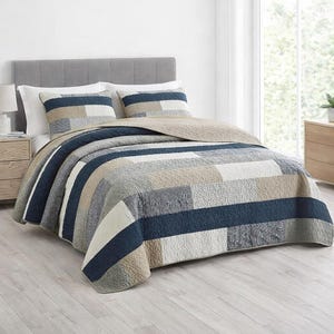 May include: A patchwork quilt set with a neutral color palette of navy blue, beige, gray, and white. The quilt features a geometric pattern with matching pillow shams. The bedding is displayed on a bed with a gray headboard.