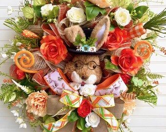 May include: A decorative Easter wreath featuring a bunny wearing a top hat and glasses, surrounded by orange and white roses, carrots, and greenery. The wreath has a large bow with a bunny print and the text "JlowsDesigns".
