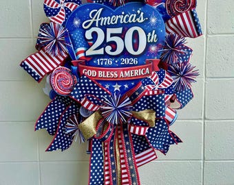 May include: A patriotic wreath with a blue heart-shaped centerpiece that reads "America's 250th 1776-2026" and "God Bless America." The wreath features red, white, and blue accents, including star-spangled ribbons, miniature American flags, and decorative elements.