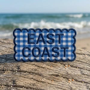May include: A rectangular patch with a scalloped edge featuring a blue and white gingham pattern. The text EAST COAST is embroidered in dark blue thread across the center of the patch in a bold, sans-serif font with a raised, textured appearance.
