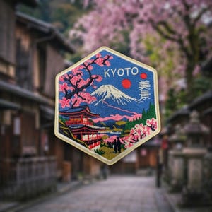 May include: A hexagonal embroidered patch featuring a blue sky, a snow-capped mountain, a red pagoda, and pink cherry blossom trees. The text KYOTO is embroidered in white at the top, with Japanese characters printed vertically on the right side.