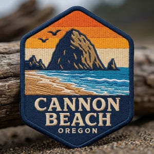 May include: A hexagonal embroidered patch featuring a landscape of Haystack Rock at Cannon Beach, Oregon. The design includes a sunset sky in orange and yellow, a blue ocean with white waves, a sandy beach, and the text CANNON BEACH OREGON.