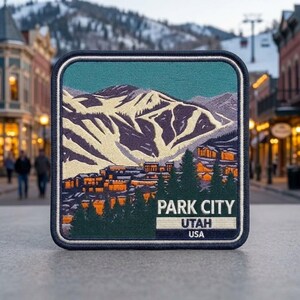 May include: A square embroidered patch featuring a mountain landscape with snow-covered slopes, a town with orange-lit buildings, and dark green pine trees. The text PARK CITY UTAH USA is embroidered in white and black at the bottom of the patch.