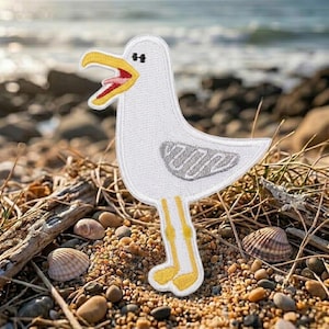May include: An embroidered patch shaped like a white seagull with a yellow beak, a red tongue, a black eye, and yellow feet. The wing features gray stitched details. The patch has a white border and is positioned upright on a textured surface.