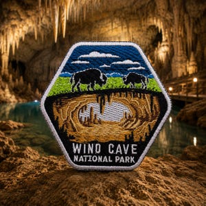 May include: A hexagonal patch featuring a landscape with two bison on green grass under a blue sky with clouds. Below, a cave illustration is visible. The text "WIND CAVE NATIONAL PARK" is at the bottom.