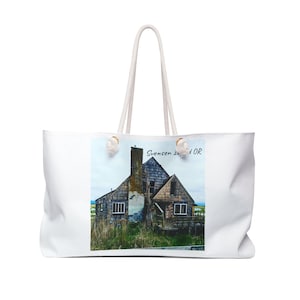 May include: White tote bag with a scenic image of a weathered wooden building with a chimney, set against a cloudy sky. The bag has white rope handles and the text "Svensen L OR".