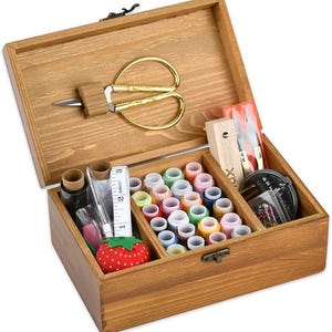 May include: A rectangular wooden sewing box with a hinged lid featuring gold-tone scissors mounted inside. The interior contains multiple spools of colourful thread, a white measuring tape, a red strawberry-shaped pincushion, and sewing tools.