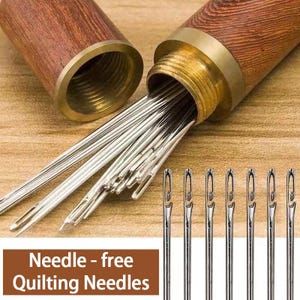 May include: A set of silver-colored metal quilting needles with open-eye tops, stored in a cylindrical wooden case with a brass-colored threaded cap. The text "Needle - free Quilting Needles" is printed in white on a brown rectangular background.