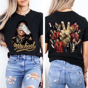 May include: Black t-shirt featuring a portrait of Michael Jackson with a sparkling glove and the name "Michael" in gold script. The back of the shirt displays a peace sign with images of Michael Jackson and a gold microphone.