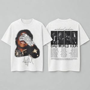 May include: White t-shirts featuring Michael Jackson. One shirt displays a portrait with a jeweled glove, the other shows a concert photo and "BAD WORLD TOUR" text. Both shirts have the singer's signature.