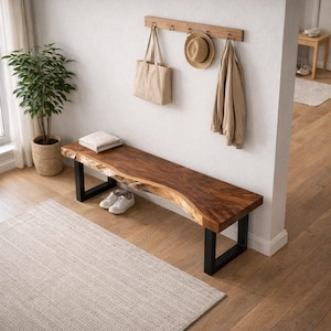 May include: A wooden bench with a live edge design and black metal legs. A beige tote bag, a straw hat, and a jacket hang on a wooden rack on the wall. A potted plant and a pair of white trainers are also visible.