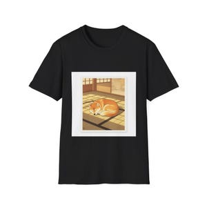 以下が含まれることがあります： 黒いTシャツ。日本の様式の部屋で眠っているオレンジと白の犬の額入りイラストが特徴です。アートワークは、畳の上に丸まっている犬を描いており、窓から差し込む日光が特徴です。