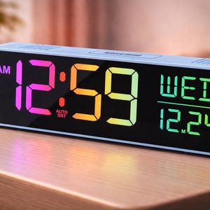 May include: A light blue digital alarm clock displaying the time as 12:59 AM, Wednesday, December 24th. The numbers are in a gradient of colors, with a black background. The clock is rectangular and sits on a wooden surface.