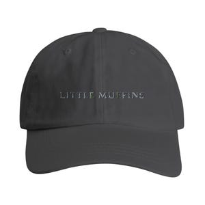 Könnte beinhalten: Dunkelgraue Baseballkappe mit dem gestickten Text "LITTLE MUFFINS" in hellgrauem Garn. Die Kappe hat einen gebogenen Schirm und einen stoffbezogenen Knopf oben.