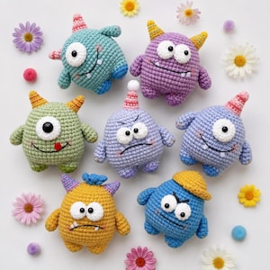 May include: Seven small, round, crocheted monster plushies in various colors including teal, purple, light green, lavender, blue, and yellow. Each monster features unique details like horns, hats, and expressive eyes, surrounded by scattered colorful flowers.