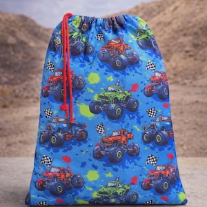 Puede incluir: Una bolsa azul con cordón con un patrón repetido de monster trucks coloridos. Los camiones son rojos, verdes, naranjas y azules, con ruedas negras y banderas a cuadros. La bolsa tiene un cordón rojo.