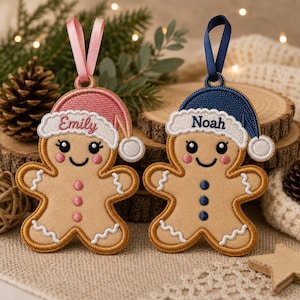 May include: Two embroidered gingerbread person ornaments with hanging ribbons. One features a pink hat with the name Emily, the other a blue hat with the name Noah. Both have white icing details, pink or blue buttons, and smiling faces.