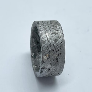 May include: A close-up of a silver ring with a distinctive, textured pattern. The ring's surface features an intricate design of interwoven lines, creating a unique visual appeal. The ring is a band style, with a solid, substantial appearance.