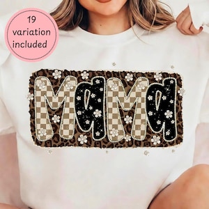 Puede incluir: Sudadera blanca con un diseño decorativo que dice "MAMA". Las letras son negras y a cuadros, con un borde de estampado de leopardo. El diseño está adornado con pequeñas flores blancas. El texto "19 variation included" en un círculo rosa.