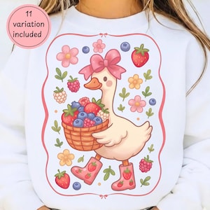 May include: White sweatshirt with a whimsical illustration of a goose wearing a pink bow and boots, carrying a basket of berries. The design includes pink flowers, strawberries, and blueberries, framed by a pink border. Text on the upper left says "11 variation included".