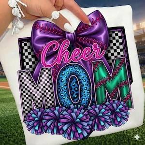 Puede incluir: Camiseta blanca con un diseño vibrante. Las palabras "Cheer Mom" están en rosa y turquesa, con un lazo morado y una "O" con estampado de leopardo. Las letras "M" tienen un patrón de cuadros blancos y negros, y hay pompones en la parte inferior.