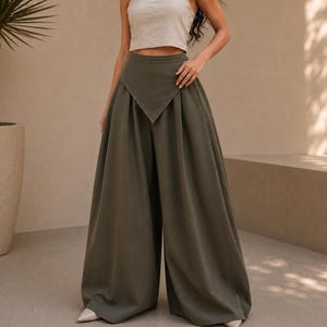 May include: Olive green high-waisted wide-leg trousers featuring a distinct V-shaped pointed front waistband detail. The pants have a voluminous, flowing silhouette with deep pleats extending from the waist down to the floor-length hemline.
