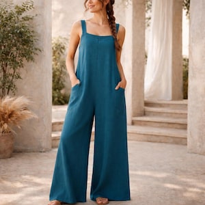 Könnte beinhalten: Ein tealfarbener Jumpsuit mit weiten Beinen und quadratischem Ausschnitt. Der Jumpsuit hat zwei Vordertaschen und breite Träger. Das Model trägt Sandalen. Der Hintergrund umfasst Säulen, Treppen und Pflanzen.
