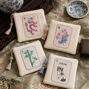May include: Four off-white zippered pouches with embroidered designs. One features a pink dragon, another a blue bird and pink flowers, a third green bamboo, and the last a dog with the word "JOKER". Each has a tassel and bead.