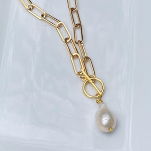Peut inclure: Un collier en chaîne dorée avec un pendentif en forme de perle ovale. La chaîne est faite de métal épais et relié et a un fermoir à bascule.