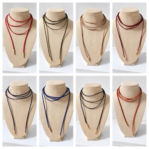 May include: A collection of eight long cord necklaces in various colors including red, olive green, tan, burgundy, navy, royal blue, black, and orange. Each necklace features a thin, soft cord wrapped multiple times and finished with gold-toned metal tips.