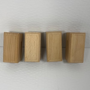 May include: Four rectangular wooden blocks arranged in a horizontal row. Each block features a light tan natural wood grain finish with a recessed rectangular panel design on the front face, showcasing a smooth, uniform texture and clean edges.