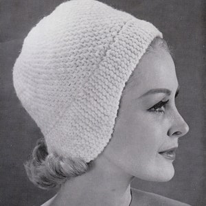 May include: A white knitted hat with a simple design. The hat is worn by a woman with blonde hair.