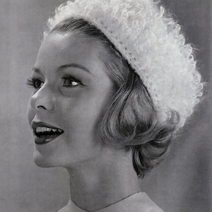 May include: A woman wearing a white crocheted hat with a fluffy texture. The hat is worn on her head and covers her ears. She is looking up and smiling.