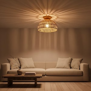 May include: A woven rattan ceiling light fixture with a warm, inviting glow. The light casts a radial pattern on the ceiling. Below, a beige sofa with matching pillows and a wooden coffee table create a cozy living room setting.