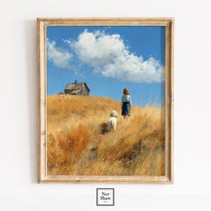 May include: A framed art print depicting a rural landscape. A person and a dog are on a hill covered in dry, golden grass. An old house is visible under a blue sky with a large white cloud. The frame is light-coloured wood.