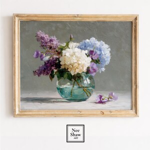 May include: A framed painting of a floral still life, depicting a glass vase with white, blue, and purple flowers. The artwork is in a gold-coloured frame and signed "Nee Shaw Art". The background is a muted grey.