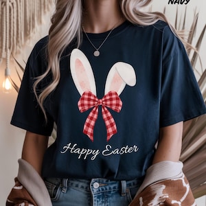 May include: Navy blue t-shirt featuring a graphic of bunny ears with a red and white plaid bow. The words "Happy Easter" are written in a script font below the graphic. The word "NAVY" is printed in the upper right corner.