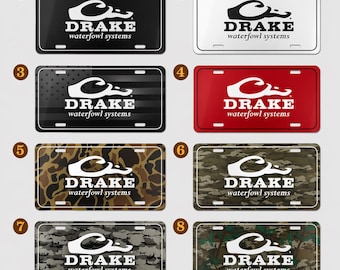 May include: A collection of license plates with the "DRAKE waterfowl systems" logo. The plates feature various designs, including solid black, white, red, camouflage, and a design with American flag stripes.
