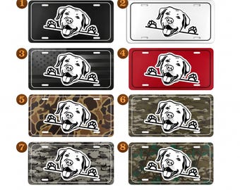 May include: A collection of license plates featuring a Labrador Retriever design. The plates come in various colors and patterns, including black, white, red, camouflage, and an American flag design. The dog graphic is in black and white.