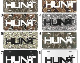 May include: License plates with the word "HUNT" in white or black block letters, and a silhouette of a deer. The plates have camouflage patterns in various colors, including green, brown, and gray. Some plates have a black or white background.