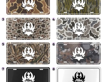 May include: Eight license plates with a white logo and the word "Hank". The plates feature camouflage patterns in various colors, including brown, green, and gray. One plate is black, and another is white.