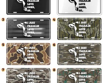 May include: License plates with the phrase "I Just Freakin Love Cows, OK." are displayed in various designs. The plates feature a cow graphic and are available in black, white, camouflage, and American flag patterns.
